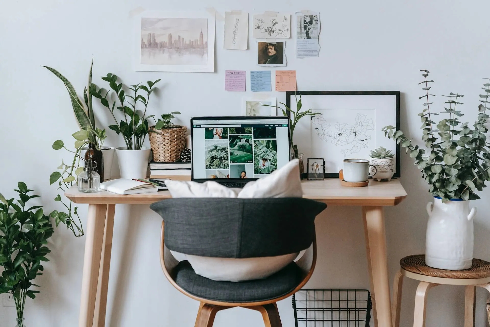 A desk with a laptop and a lot of plants around the desk.