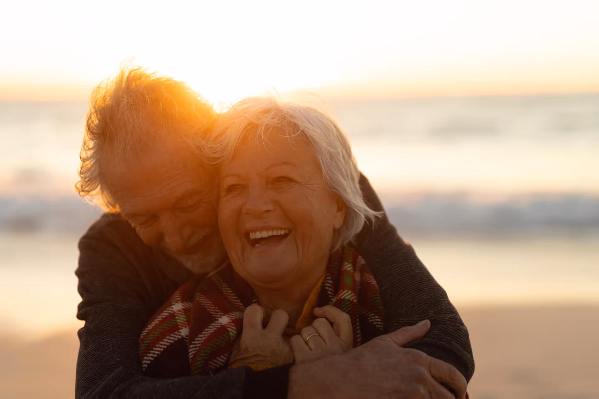 An older couple hugging and smiling with the sunset.