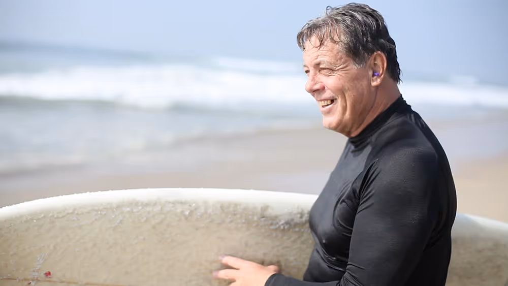 A man at the beach looking to the side with the ocean behind him.