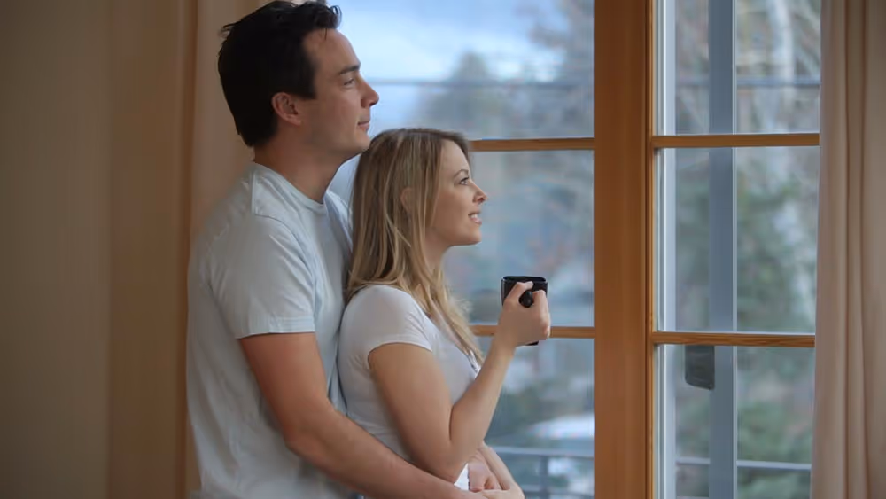 A couple looking out a window on a gloomy day with a mug.