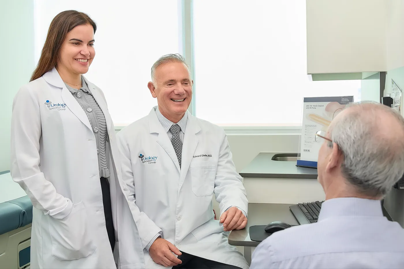 Dr. Edward Gheiler and a member of his care team talking with a patient in an exam room.